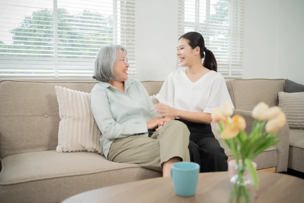 Older woman and younger woman chatting on a sofa, with a vase of flowers on the table