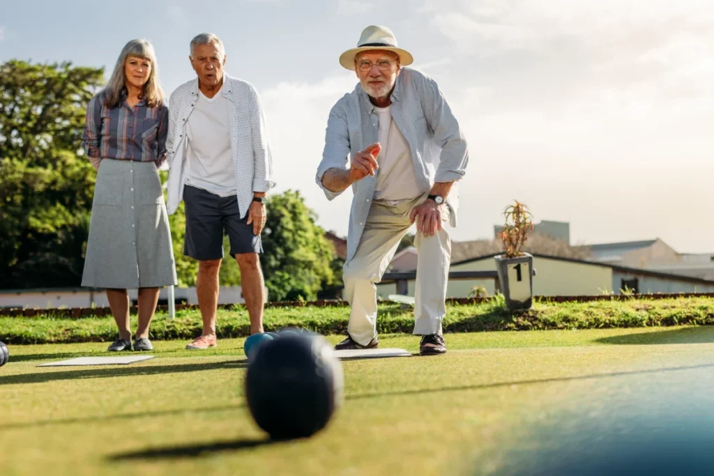 Three older adults playing a lawn ball game on a well-kept grass court