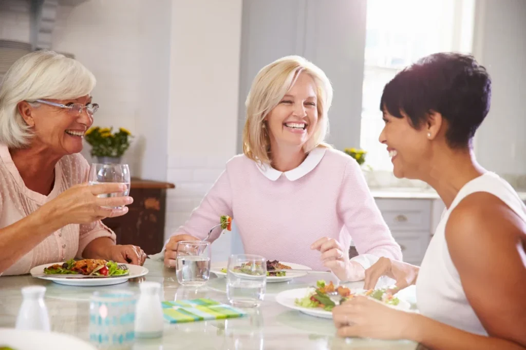Three women dining and toasting at a table with plates of salad