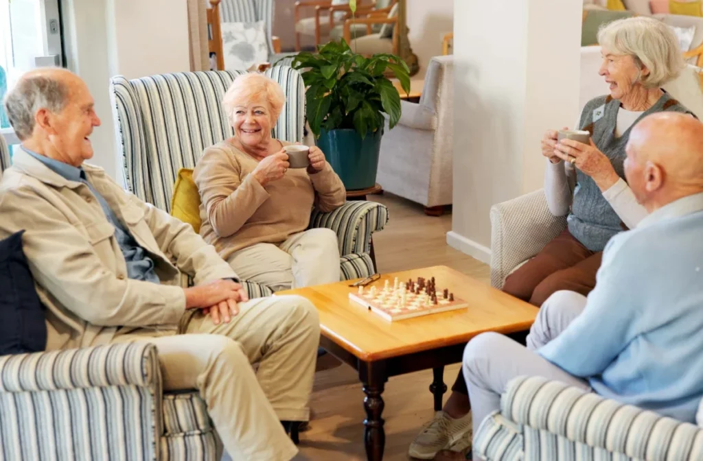 Group of older adults chatting around a chess board in a sitting room