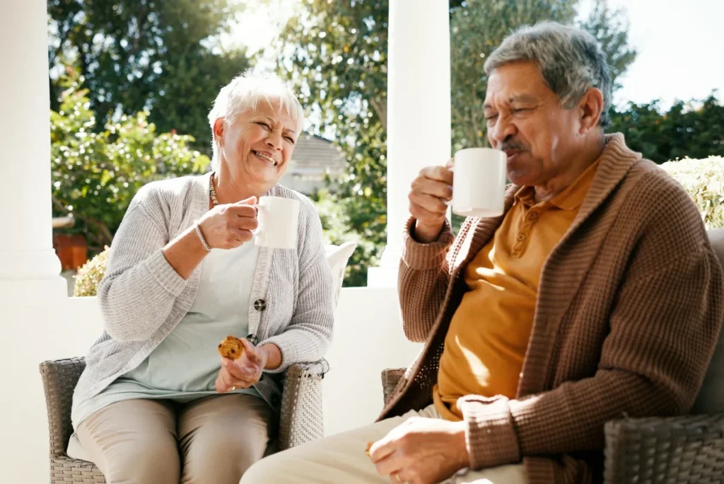 Older woman and man laughing while holding mugs on a porch