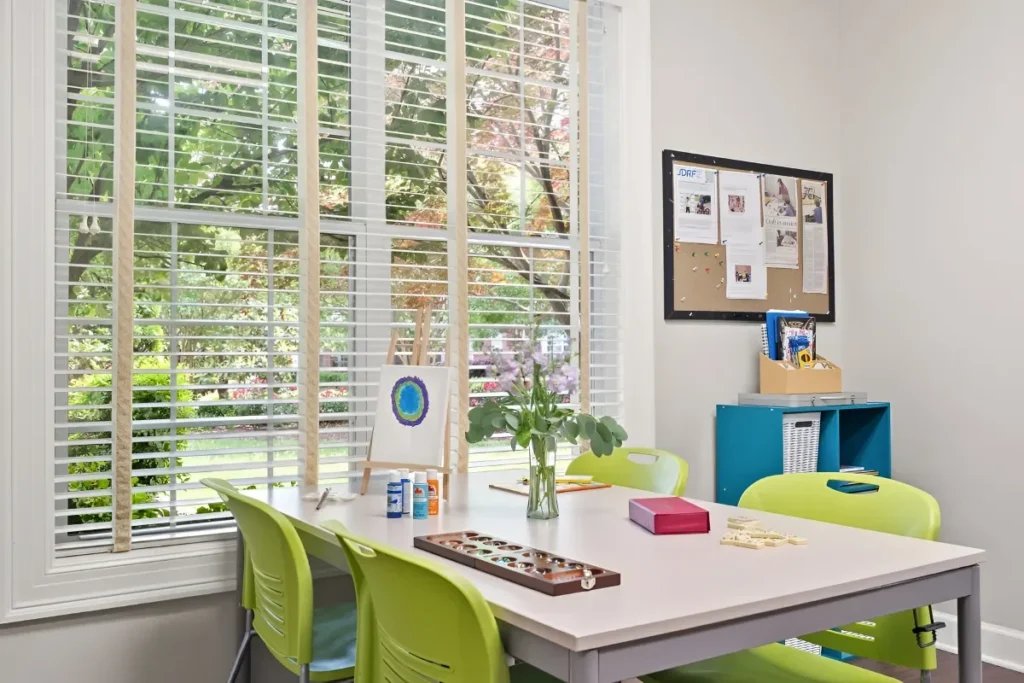 Activity table with a game board, colorful chairs and a bulletin board by a bright window
